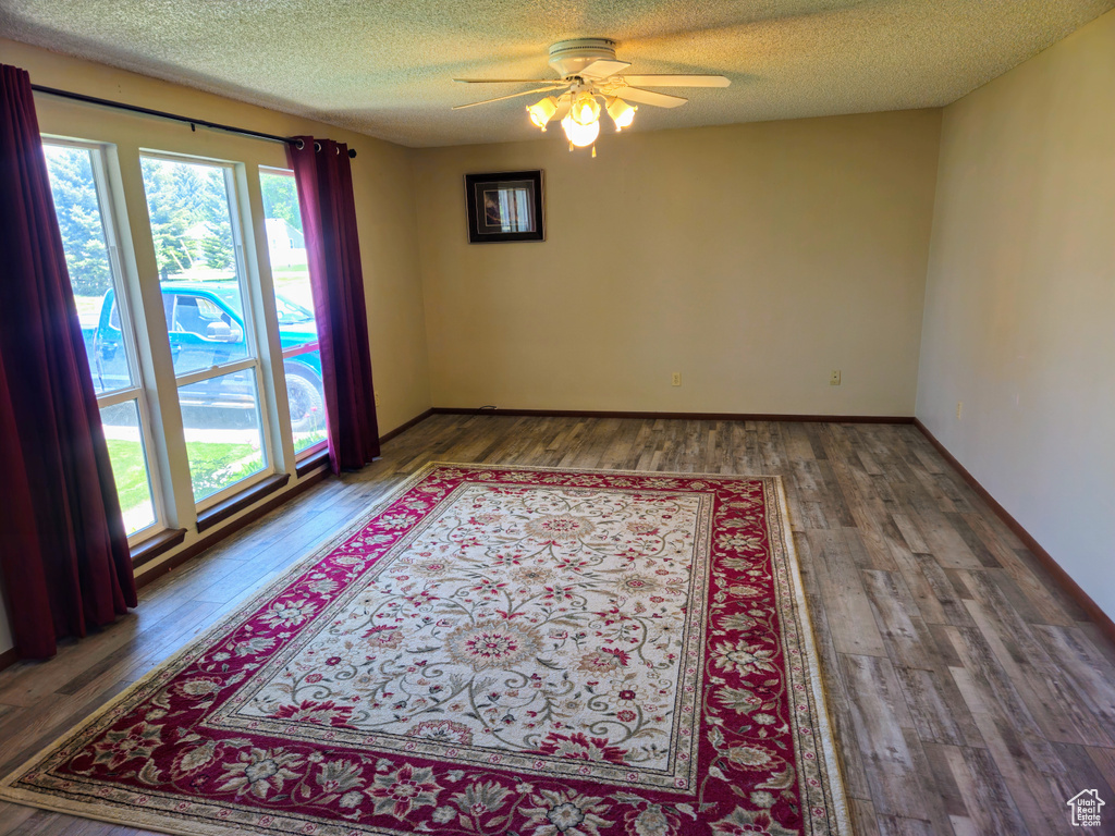 Empty room featuring healthy amount of natural light, a ceiling fan, wood finished floors, and a textured ceiling