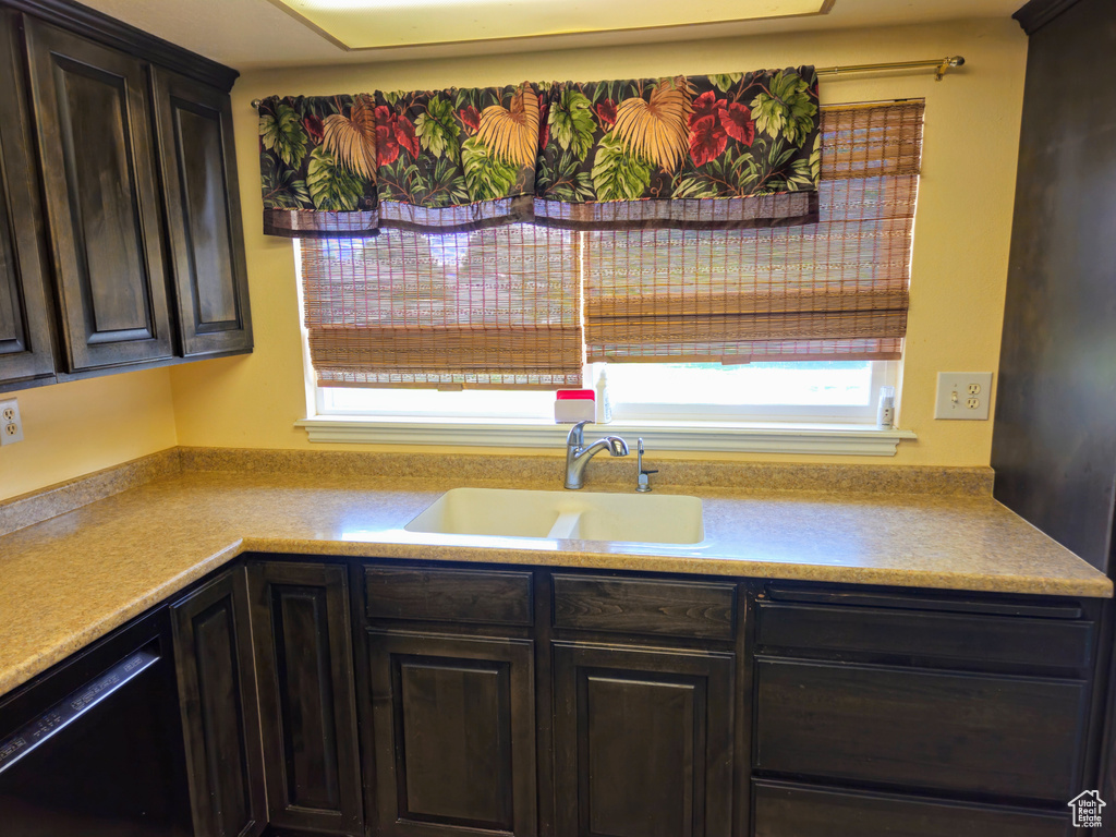 Kitchen with a sink, dishwasher, light countertops, and dark brown cabinets