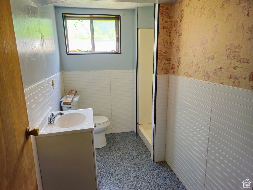 Bathroom featuring a wainscoted wall, toilet, vanity, a stall shower, and wallpapered walls
