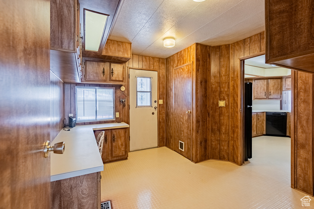 Kitchen featuring black appliances, wood walls, light countertops, and brown cabinetry