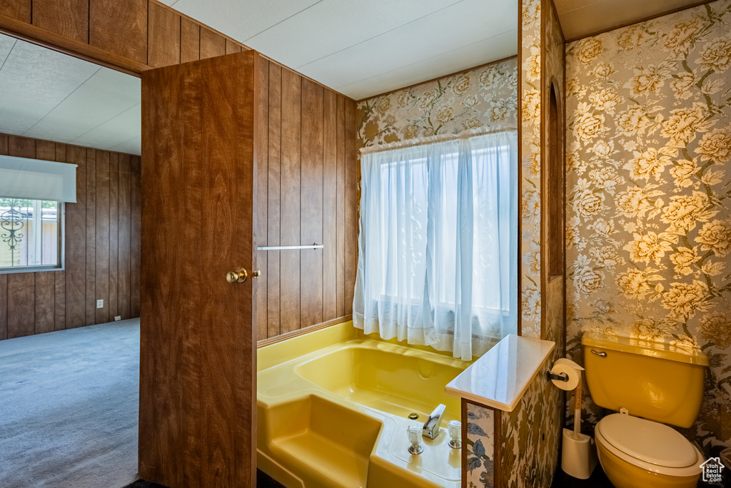Full bath featuring a bath, wood walls, and toilet