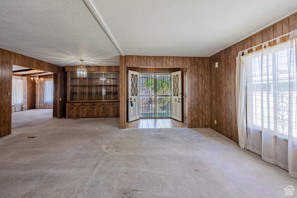 Unfurnished living room featuring a chandelier, wooden walls, a textured ceiling, and carpet
