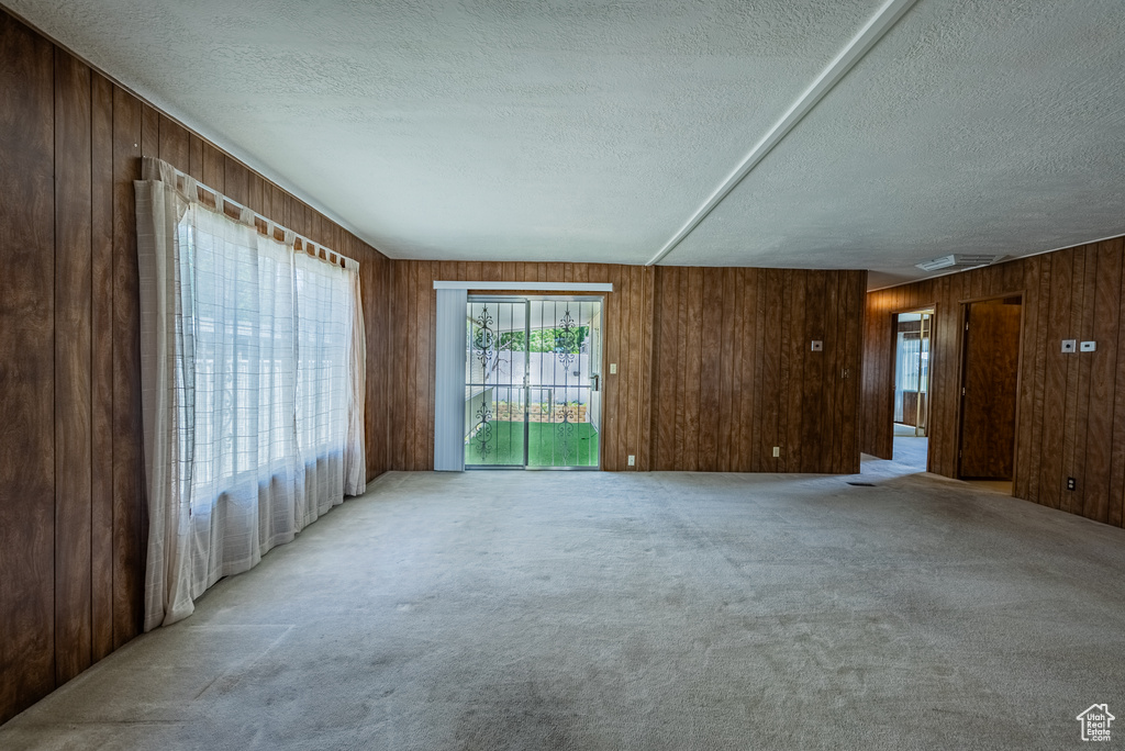 Unfurnished living room featuring a textured ceiling, carpet floors, and wooden walls