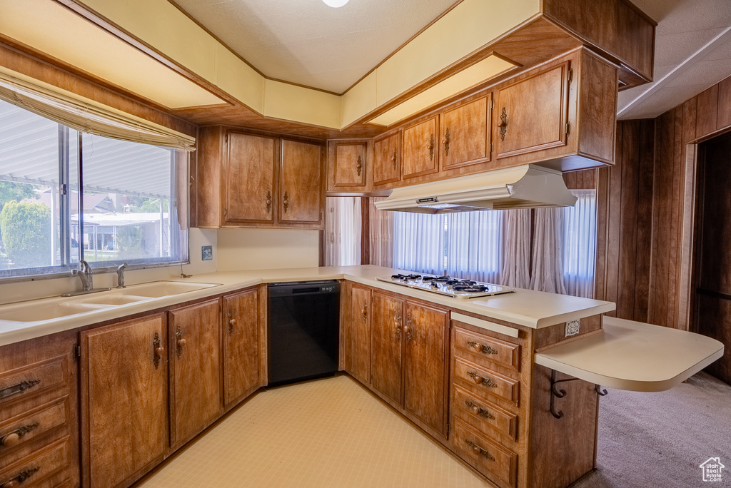 Kitchen featuring black dishwasher, under cabinet range hood, a sink, a peninsula, and brown cabinetry