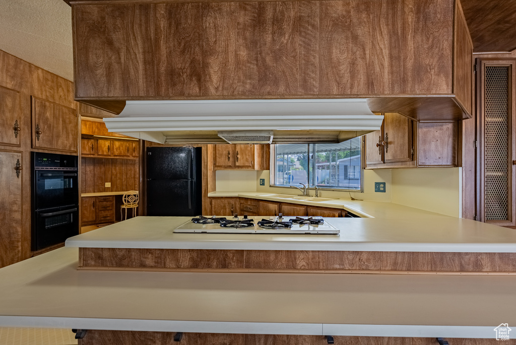Kitchen with black appliances, a sink, light countertops, brown cabinets, and a peninsula