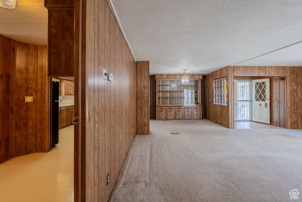 Unfurnished living room with wood walls, a textured ceiling, and light carpet