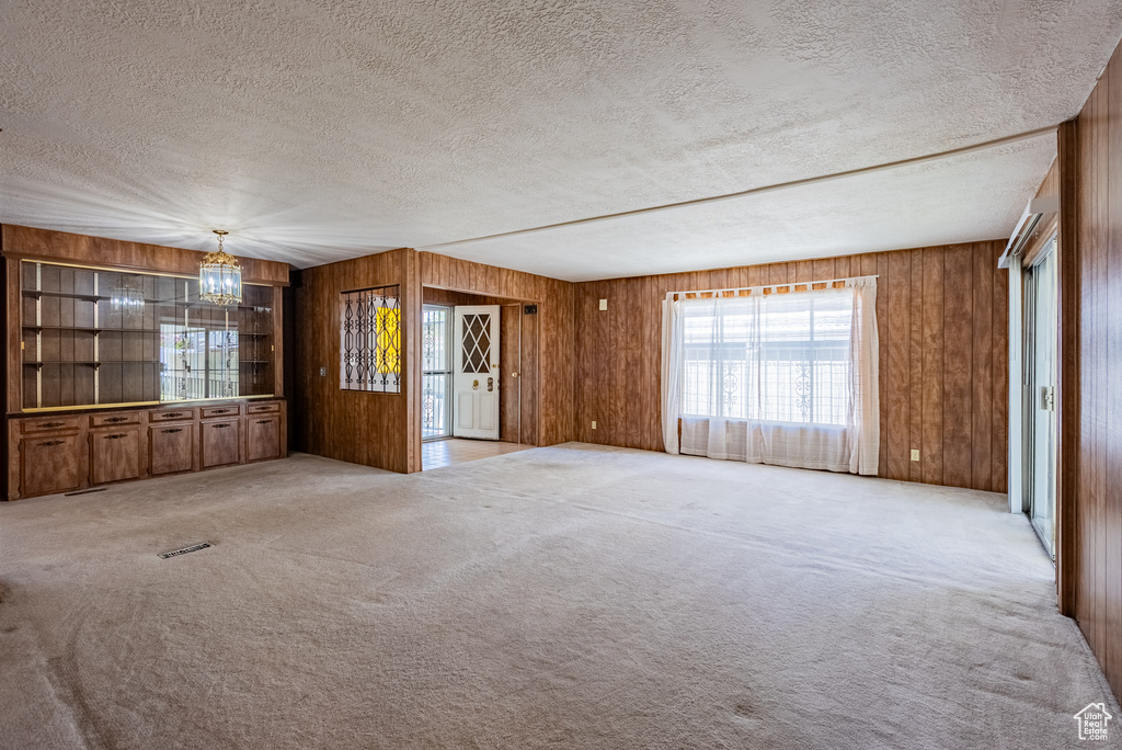 Unfurnished room with a chandelier, a textured ceiling, wooden walls, and light carpet
