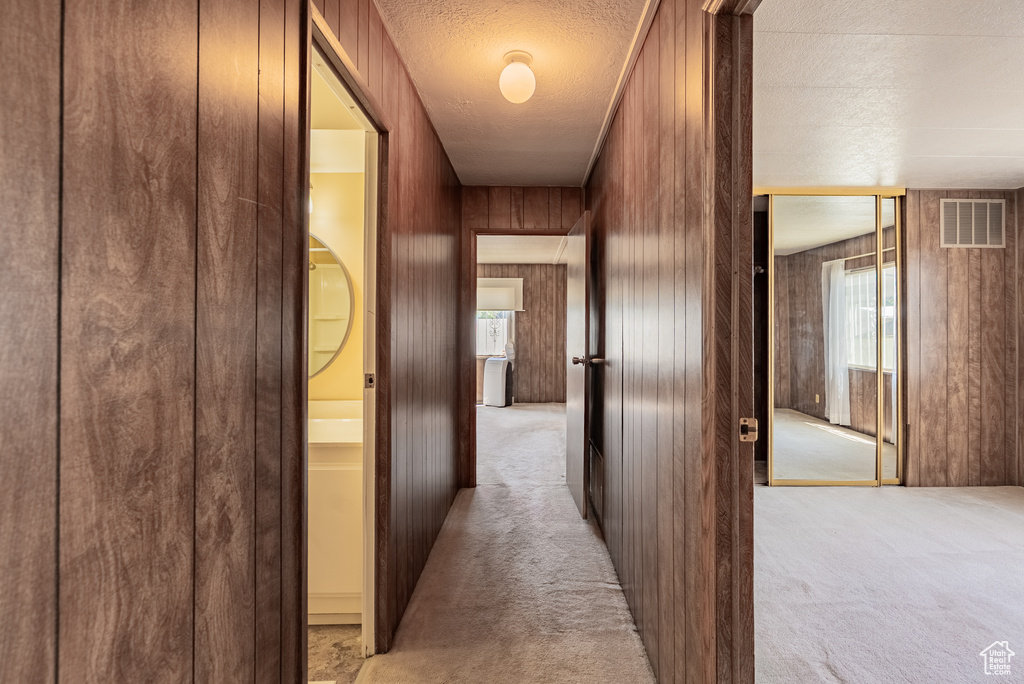 Hall featuring light colored carpet, a textured ceiling, and wood walls