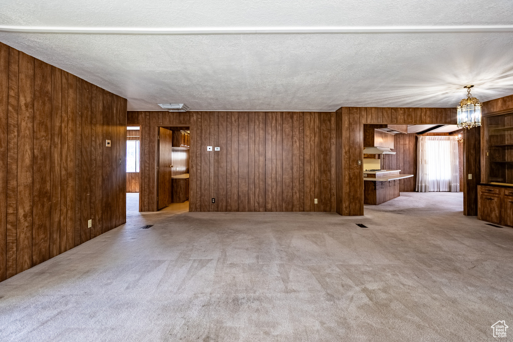 Unfurnished living room featuring wooden walls, carpet flooring, and a chandelier