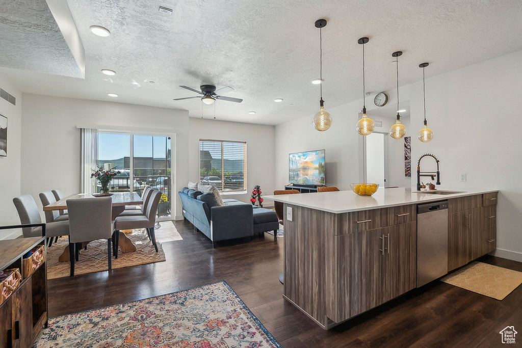 Kitchen with stainless steel dishwasher, a sink, a textured ceiling, dark wood-style floors, and light countertops