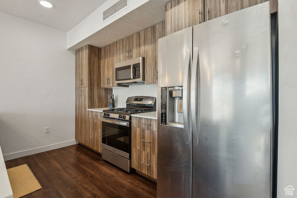 Kitchen featuring appliances with stainless steel finishes, brown cabinetry, light countertops, baseboards, and dark wood finished floors