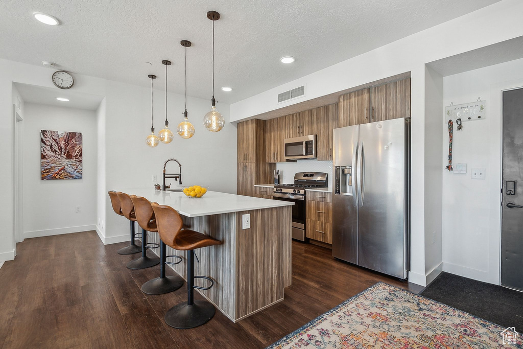 Kitchen with appliances with stainless steel finishes, brown cabinetry, a breakfast bar area, dark wood finished floors, and recessed lighting