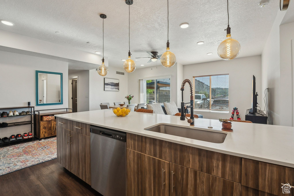 Kitchen featuring stainless steel dishwasher, a sink, light countertops, dark wood-type flooring, and a textured ceiling