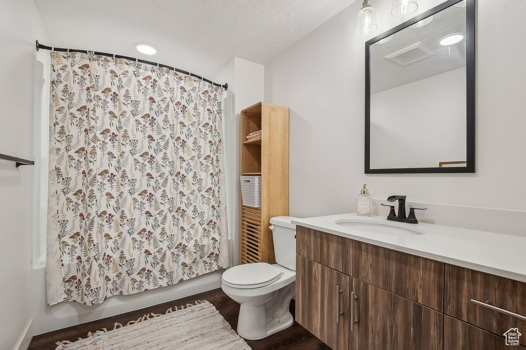Bathroom with vanity, toilet, wood finished floors, shower / tub combo with curtain, and a textured ceiling