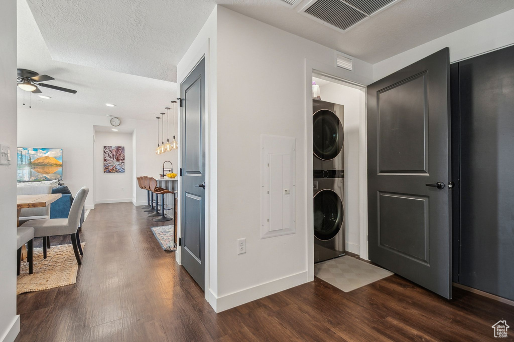 Laundry room with stacked washer and clothes dryer, dark wood finished floors, a ceiling fan, and baseboards