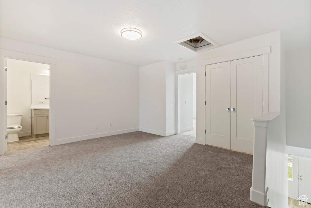 Unfurnished bedroom with light colored carpet, connected bathroom, baseboards, and a closet