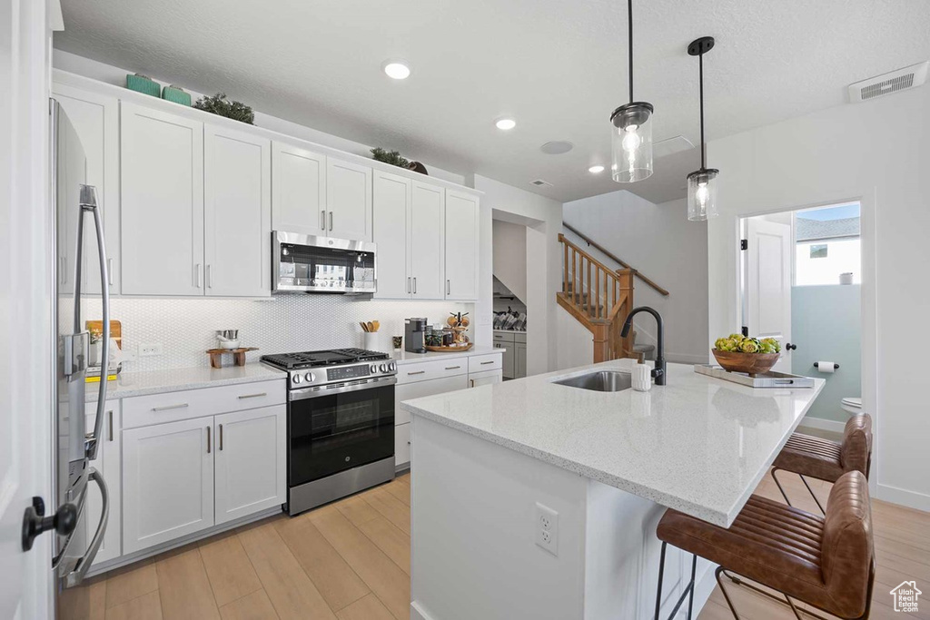 Kitchen featuring appliances with stainless steel finishes, a sink, light wood-type flooring, a center island with sink, and white cabinetry