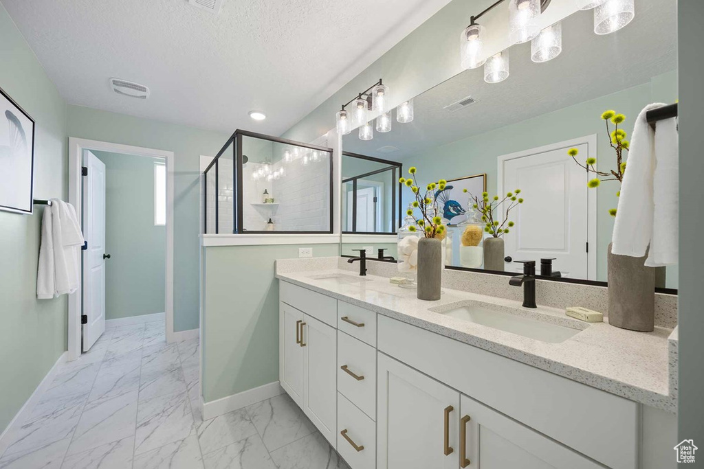 Full bath with double vanity, baseboards, marble finish floors, a shower stall, and a textured ceiling