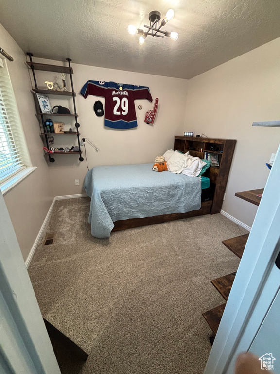 Bedroom featuring a textured ceiling, carpet, a chandelier, and baseboards