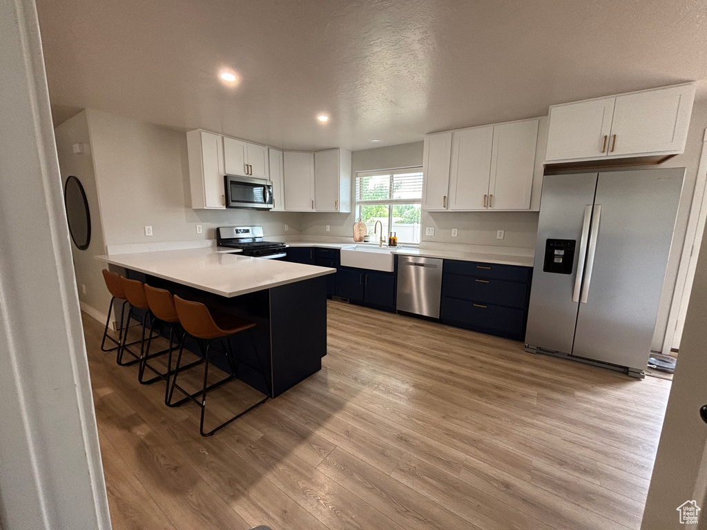 Kitchen with appliances with stainless steel finishes, a sink, light wood-style flooring, white cabinets, and light countertops