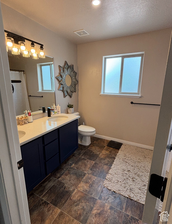 Bathroom featuring double vanity, toilet, a shower with shower curtain, baseboards, and stone finish flooring