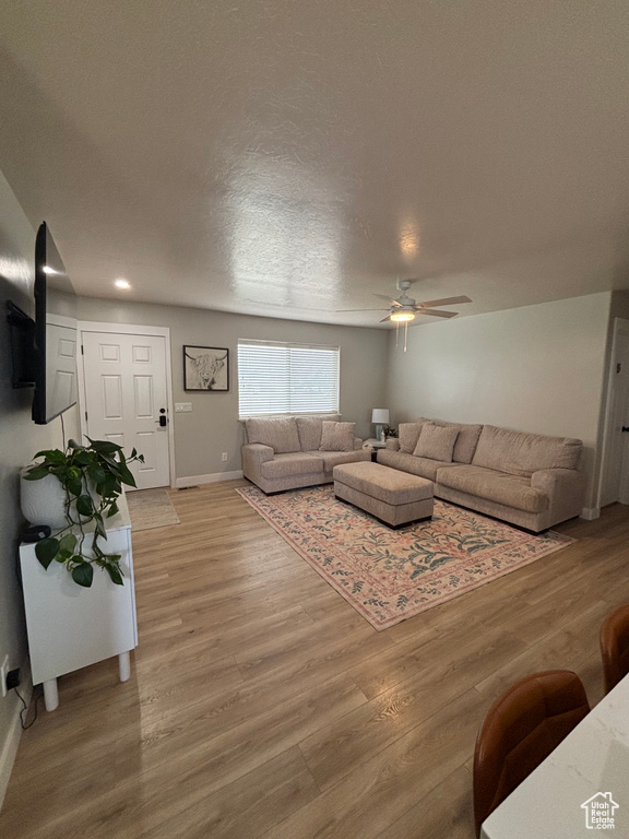 Living area featuring a ceiling fan, light wood finished floors, baseboards, and a textured ceiling