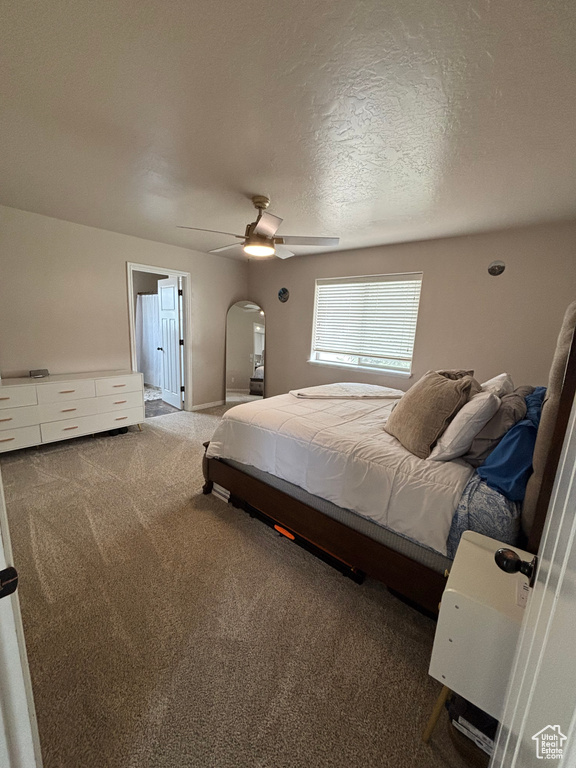 Carpeted bedroom with arched walkways, ceiling fan, and a textured ceiling