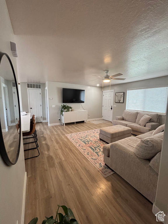 Living room featuring ceiling fan, wood finished floors, baseboards, and a textured ceiling