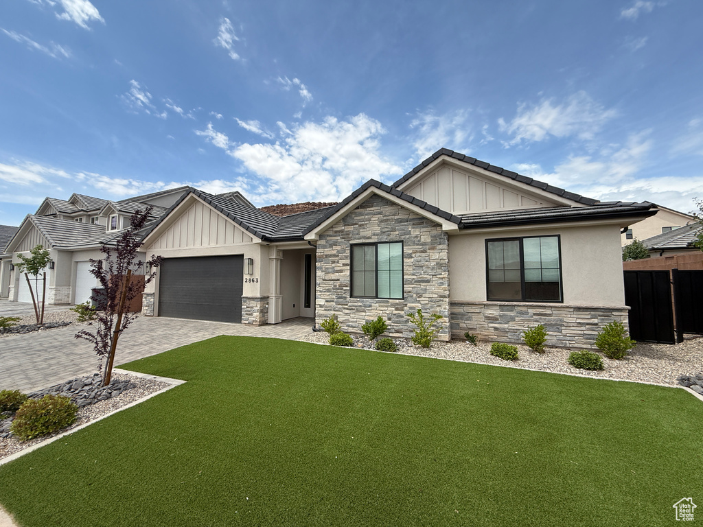 View of front facade featuring stone siding, board and batten siding, an attached garage, and decorative driveway