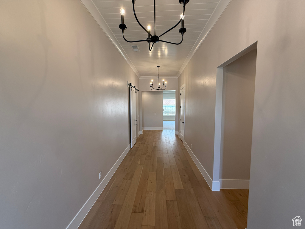 Hall featuring a chandelier, crown molding, a barn door, hardwood / wood-style flooring, and baseboards