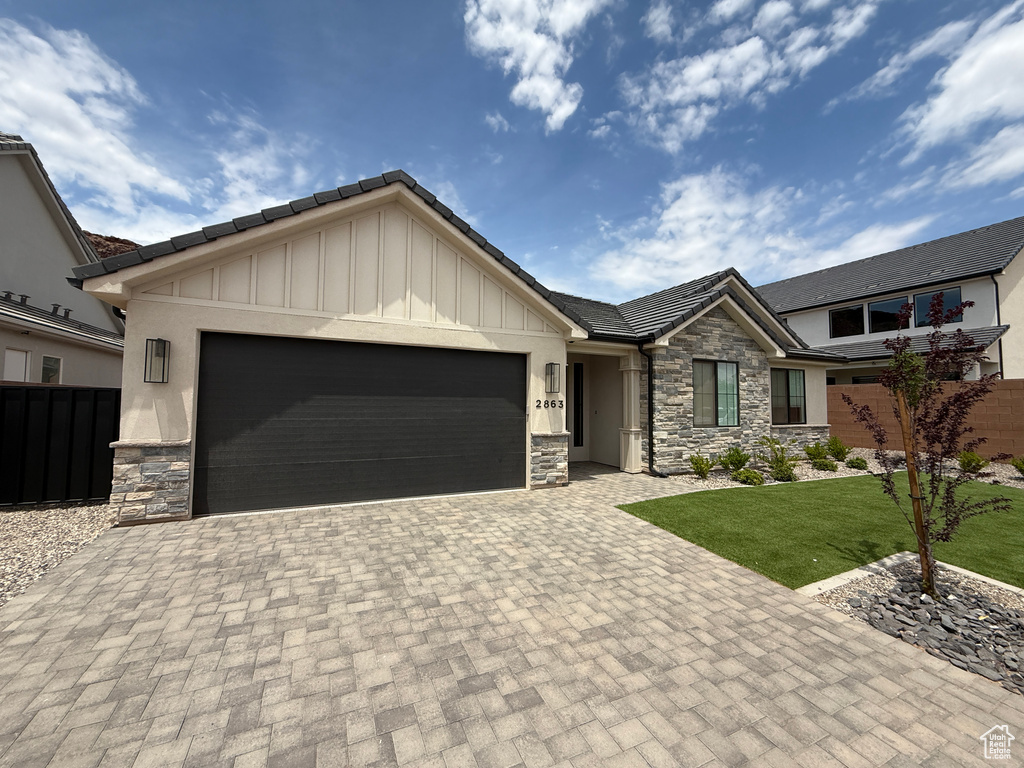 Craftsman-style house featuring stone siding, a tiled roof, an attached garage, board and batten siding, and decorative driveway