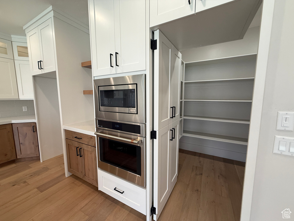Kitchen with stainless steel appliances, open shelves, light wood-style floors, and white cabinets