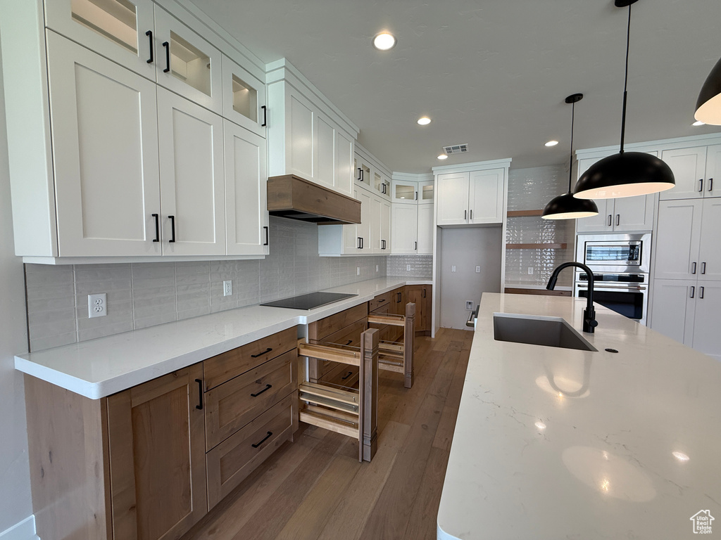Kitchen with a sink, stainless steel appliances, wood finished floors, backsplash, and glass insert cabinets