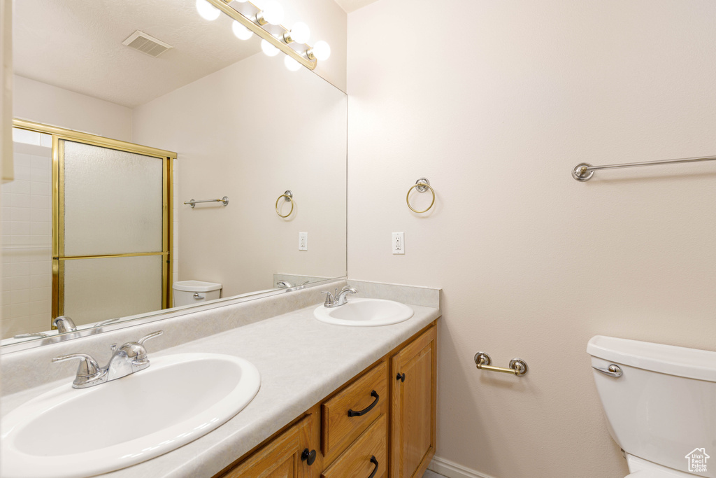 Bathroom featuring toilet, double vanity, a shower with shower door, and baseboards