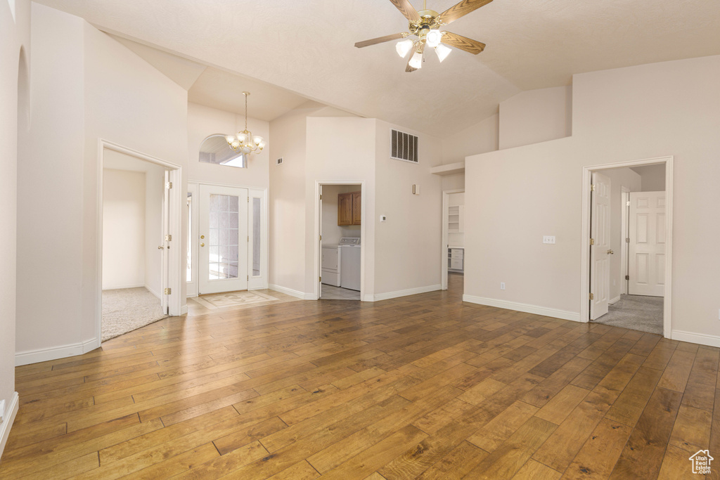 Unfurnished living room featuring hardwood / wood-style flooring, ceiling fan, a chandelier, high vaulted ceiling, and baseboards