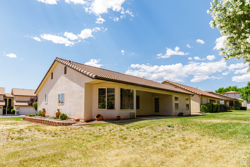 Back of house featuring a tiled roof, a yard, and stucco siding