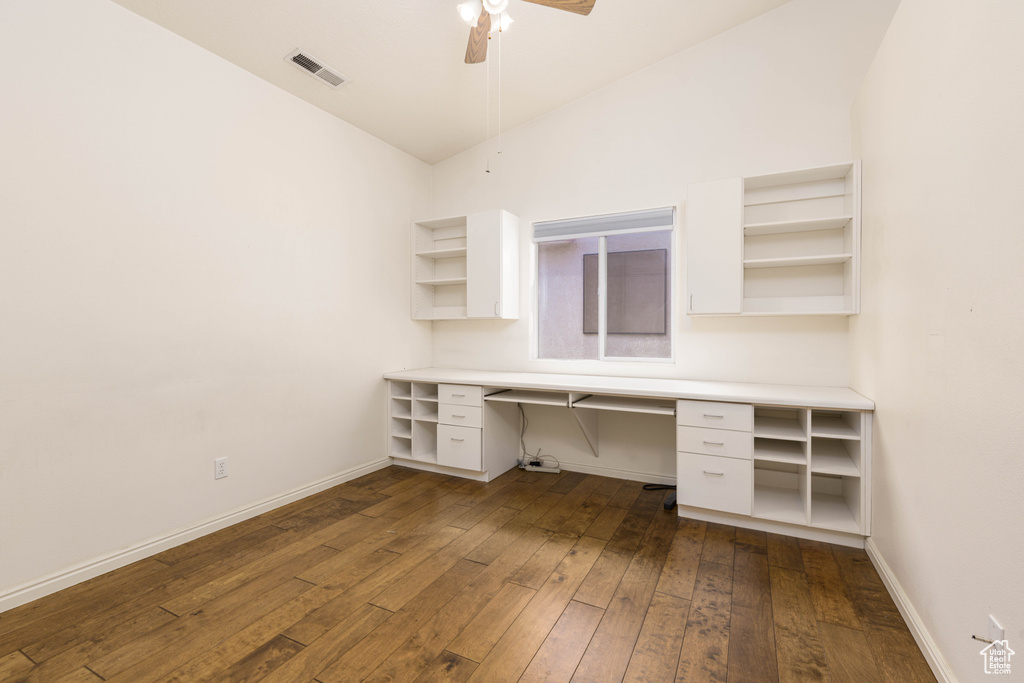 Unfurnished office featuring built in study area, dark wood finished floors, ceiling fan, baseboards, and vaulted ceiling