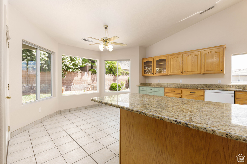 Kitchen with white dishwasher, ceiling fan, healthy amount of natural light, light stone countertops, and vaulted ceiling