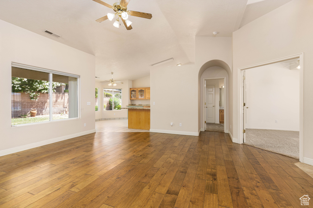 Unfurnished living room featuring ceiling fan, arched walkways, hardwood / wood-style flooring, and vaulted ceiling