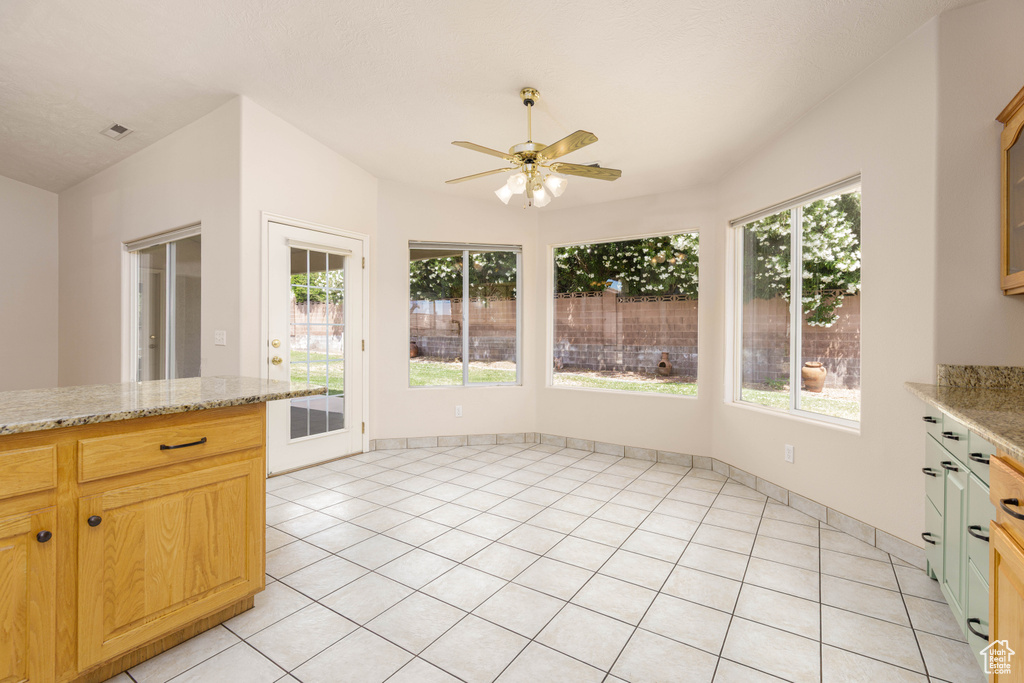 Kitchen with ceiling fan, light tile patterned flooring, and light stone countertops