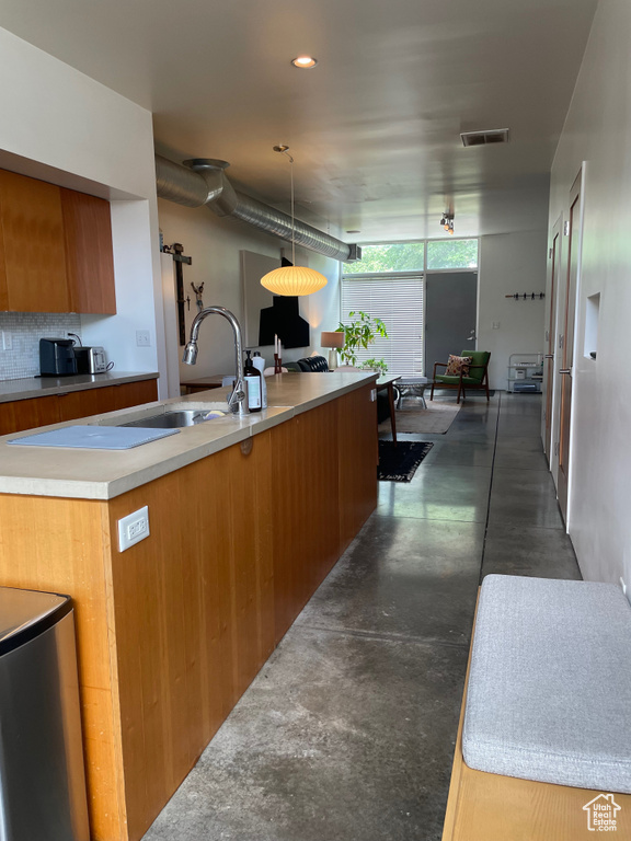 Kitchen featuring finished concrete flooring, brown cabinetry, modern cabinets, light countertops, and hanging light fixtures