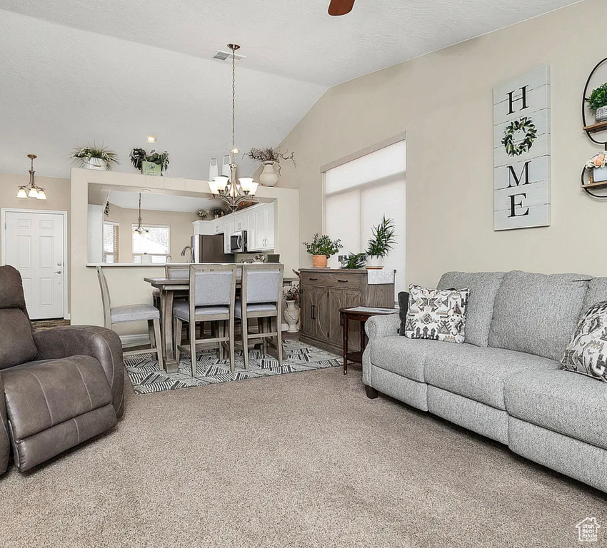 Living area featuring a chandelier, carpet flooring, vaulted ceiling, and ceiling fan