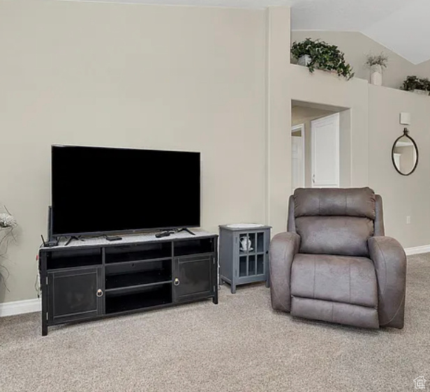 Carpeted living area featuring baseboards and vaulted ceiling