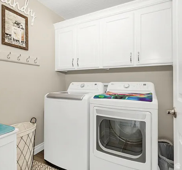 Laundry area with separate washer and dryer, cabinet space, wood finished floors, and baseboards