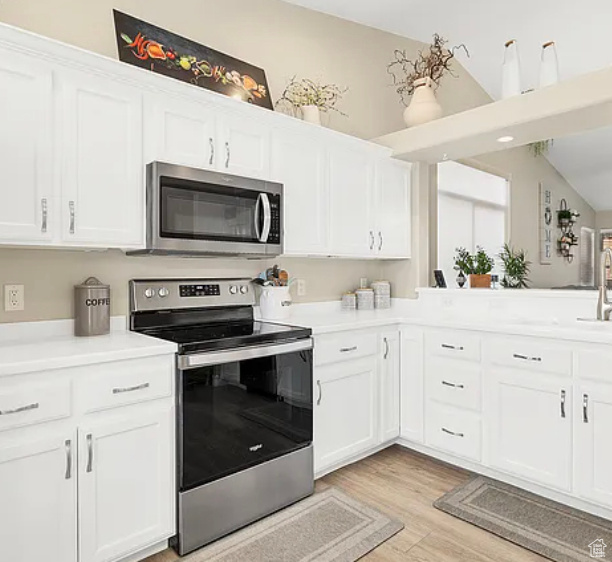 Kitchen featuring stainless steel appliances, light wood finished floors, light countertops, and white cabinetry