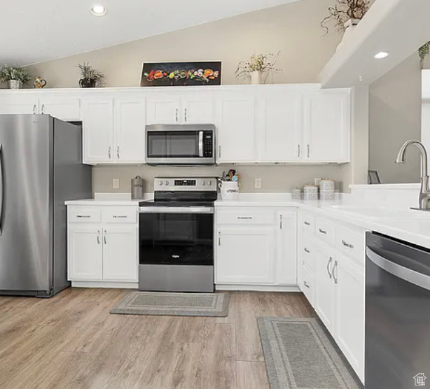 Kitchen featuring stainless steel appliances, lofted ceiling, white cabinetry, light countertops, and light wood-style floors