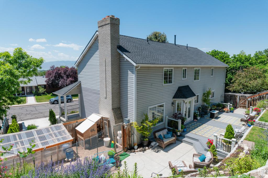 Rear view of property with a chimney, a patio area, an outbuilding, a shingled roof, and an exterior structure