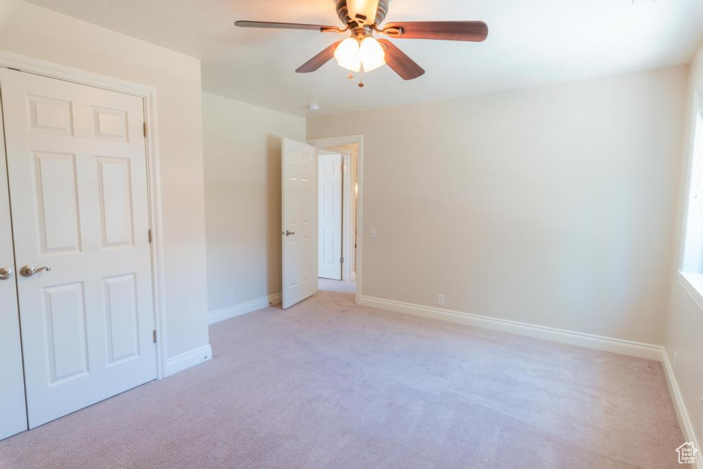 Unfurnished bedroom with light carpet, baseboards, and a ceiling fan