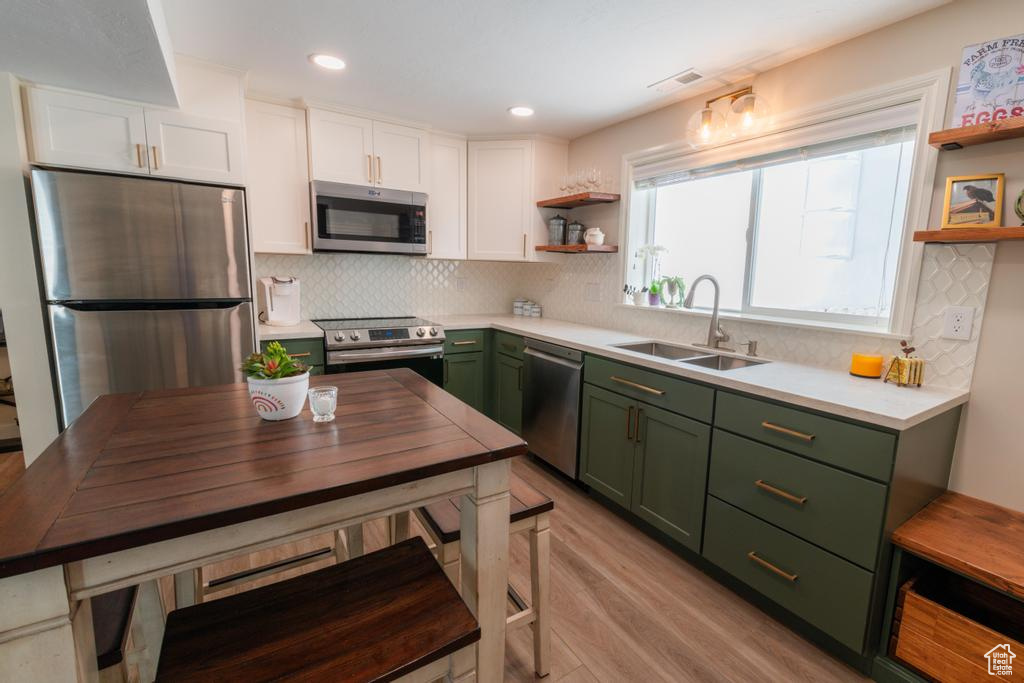 Kitchen with green cabinets, appliances with stainless steel finishes, open shelves, a sink, and recessed lighting