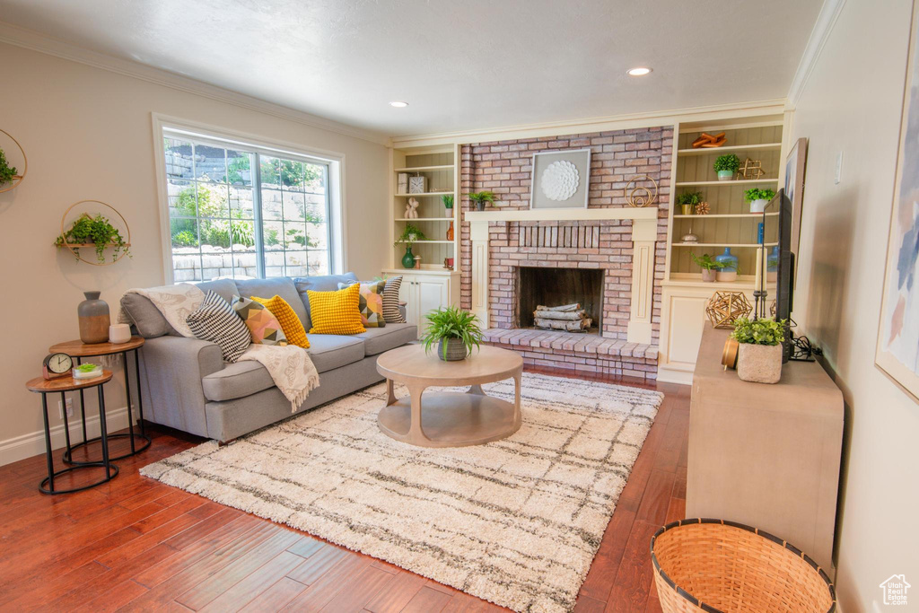 Living room with wood-type flooring, crown molding, built in shelves, a fireplace, and baseboards